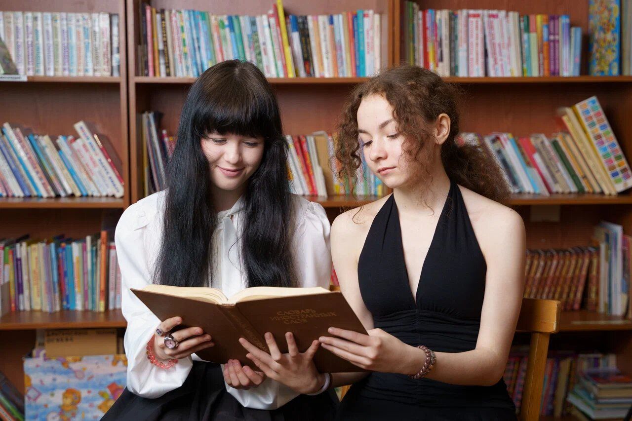 Две выпускницы с книгой у стеллажей
