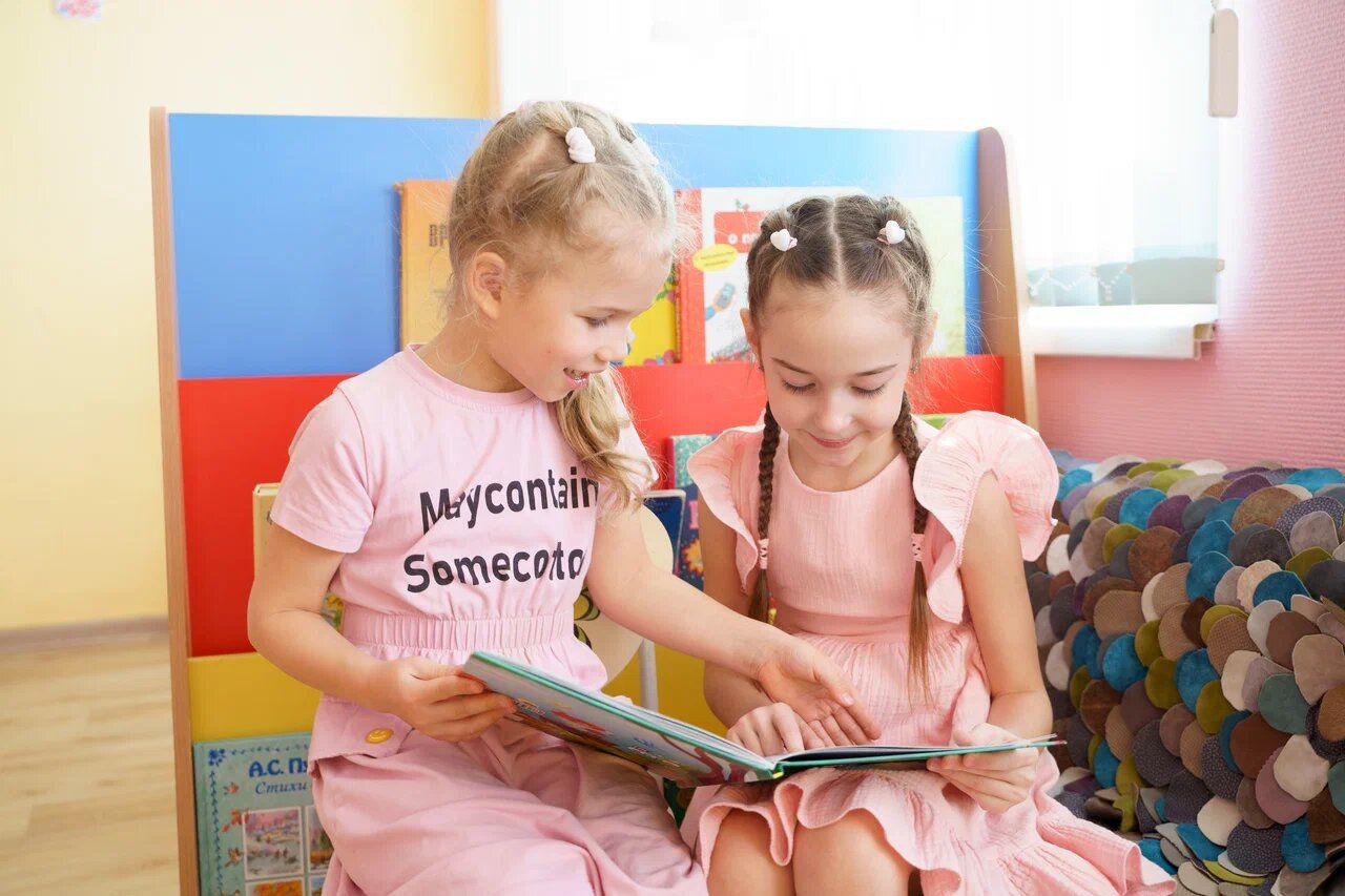 Две девочки читают книгу на диване в детском саду