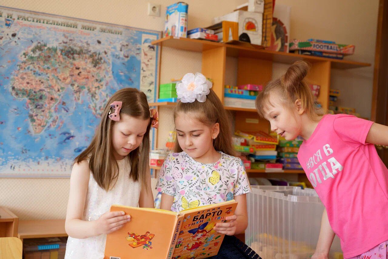 Девочки читают книгу у книжных полок в группе детского сада